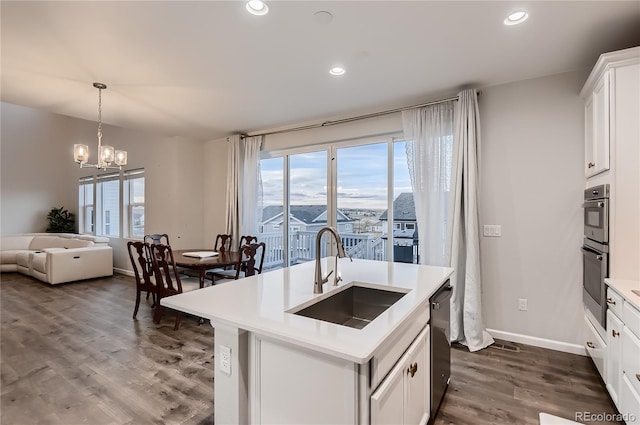 kitchen with appliances with stainless steel finishes, sink, white cabinets, dark wood-type flooring, and a center island with sink