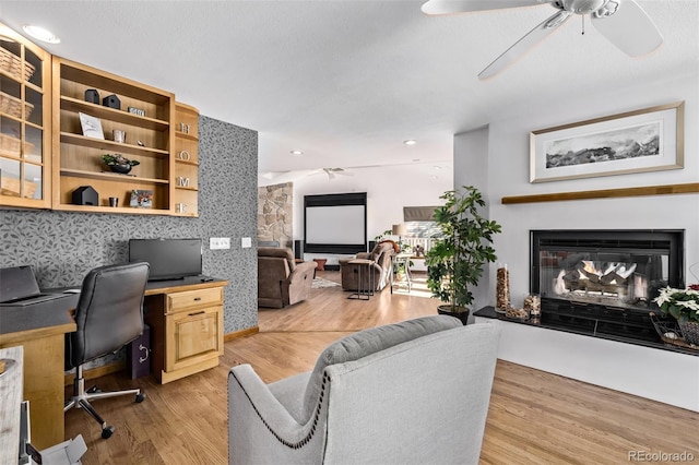 office with a ceiling fan, a glass covered fireplace, wood finished floors, and built in study area