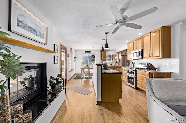 kitchen with dark countertops, appliances with stainless steel finishes, ceiling fan, and light wood finished floors