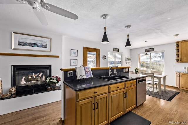kitchen with ceiling fan, dark countertops, stainless steel dishwasher, a sink, and light wood-style floors
