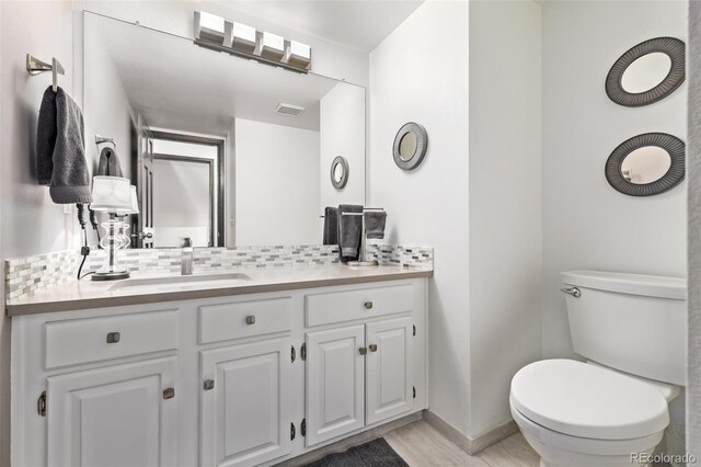 bathroom featuring vanity, decorative backsplash, visible vents, toilet, and baseboards