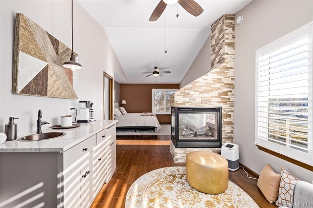 bedroom with vaulted ceiling, a tiled fireplace, a sink, and dark wood finished floors