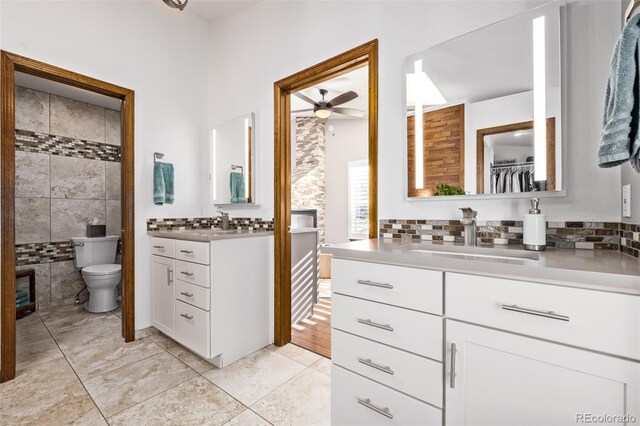 full bath with a sink, a ceiling fan, toilet, and two vanities