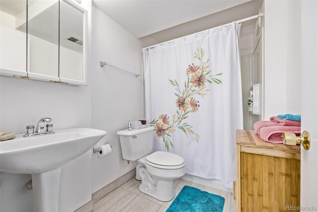 bathroom with a sink, toilet, a shower with shower curtain, baseboards, and visible vents