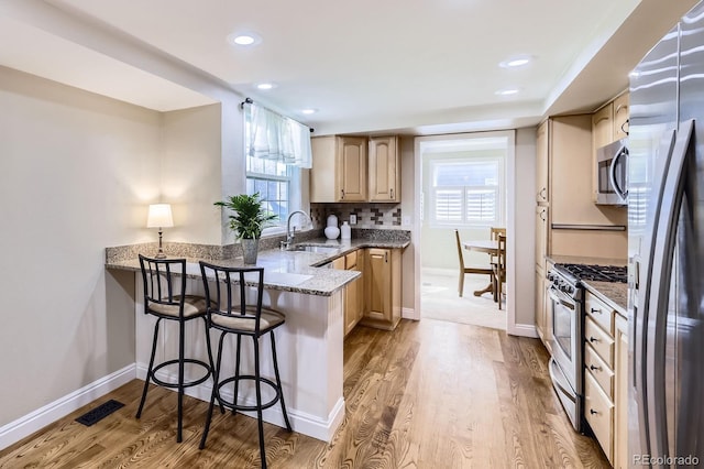 8985 W Quarto Pl, Littleton, CO 80128 - kitchen with stainless steel appliances, a peninsula, light wood-style floors, a breakfast bar area, and recessed lighting