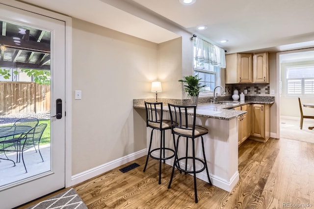 8985 W Quarto Pl, Littleton, CO 80128 - kitchen with light wood-style floors, a kitchen breakfast bar, light brown cabinetry, stone countertops, and recessed lighting