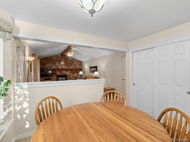 dining space with a stone fireplace, ceiling fan, and lofted ceiling with beams