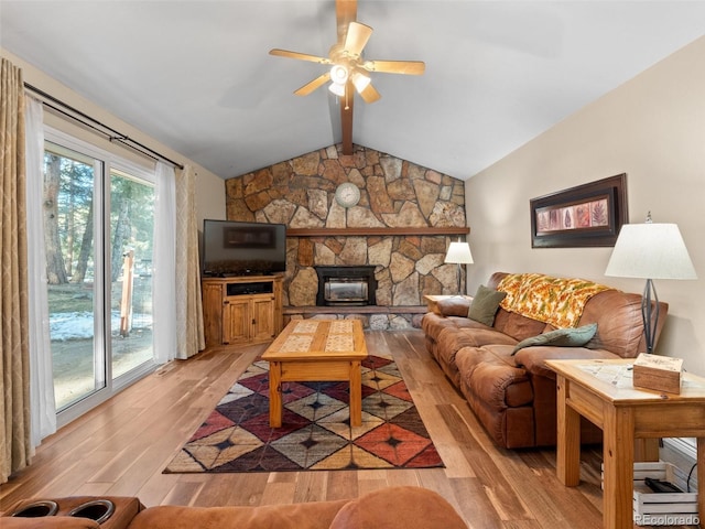 living room featuring lofted ceiling with beams, light hardwood / wood-style floors, a stone fireplace, and ceiling fan