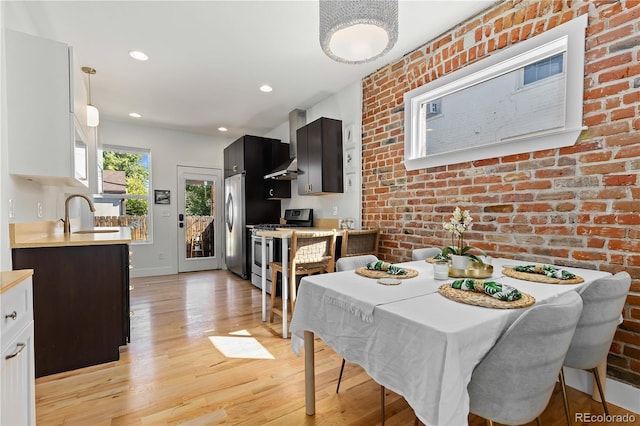 dining space with sink, light wood-type flooring, and brick wall