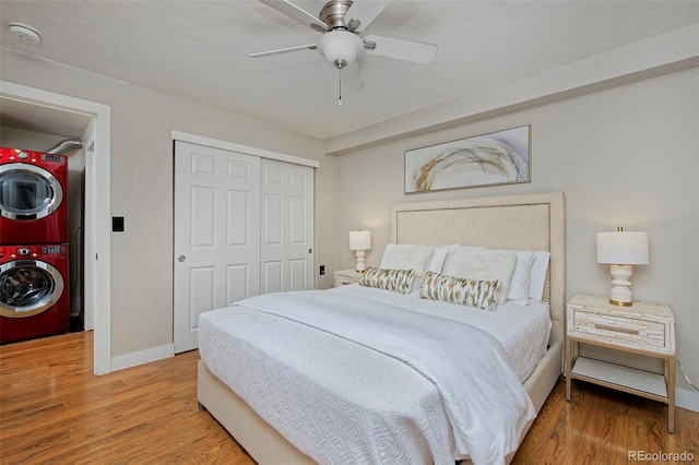 bedroom with stacked washer and dryer, wood-type flooring, ceiling fan, and a closet