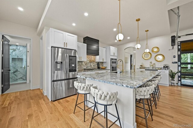 14950 W 32nd Ave, Golden, CO 80401 - kitchen featuring stainless steel appliances, a kitchen bar, decorative backsplash, light wood-style floors, and white cabinetry