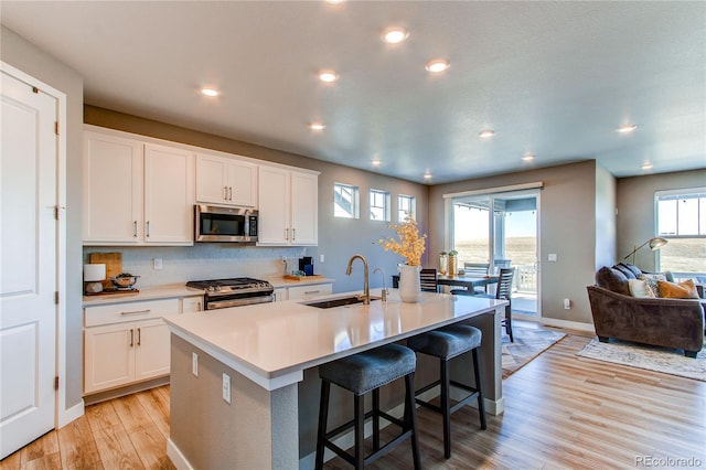 kitchen featuring appliances with stainless steel finishes, white cabinetry, light hardwood / wood-style flooring, a center island with sink, and sink