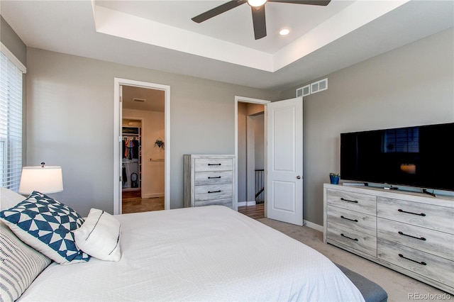 carpeted bedroom featuring a walk in closet, ceiling fan, and a raised ceiling