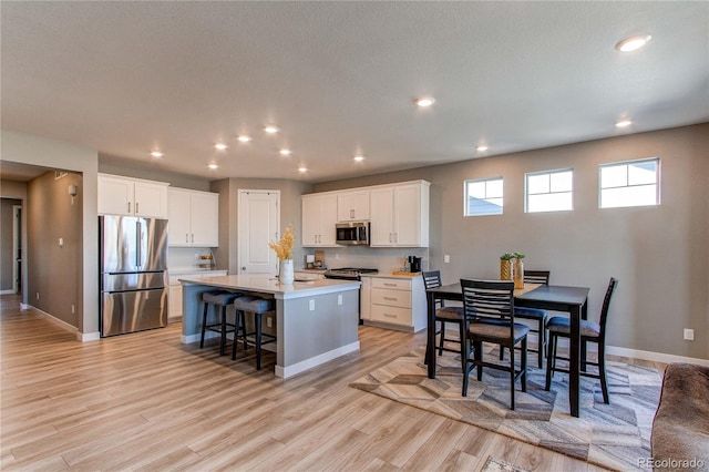 kitchen featuring white cabinets, a center island with sink, appliances with stainless steel finishes, a breakfast bar, and light hardwood / wood-style floors