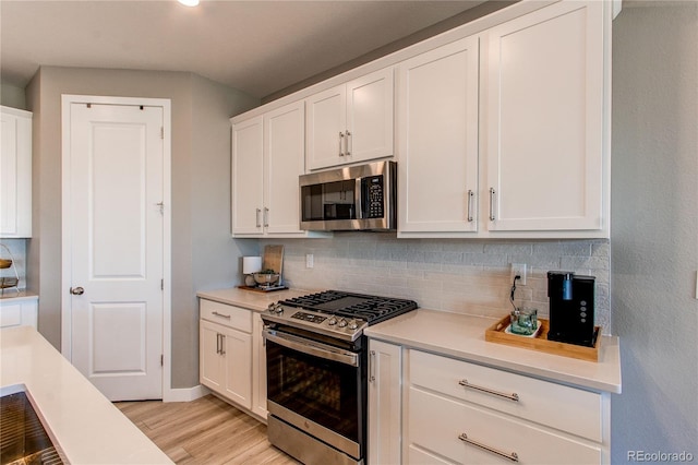 kitchen with white cabinets, stainless steel appliances, light wood-type flooring, and tasteful backsplash