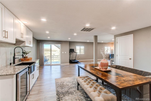 dining room with light wood-type flooring, beverage cooler, and sink