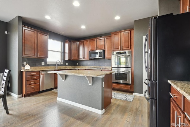 kitchen featuring a breakfast bar, a kitchen island, appliances with stainless steel finishes, brown cabinets, and light wood finished floors