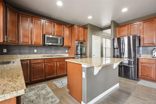 kitchen with a center island, light stone countertops, stainless steel appliances, light wood-type flooring, and backsplash