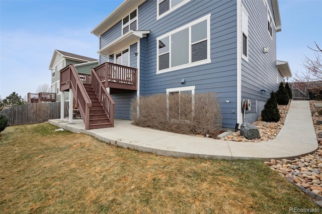 rear view of house featuring stairway, a wooden deck, fence, and a yard