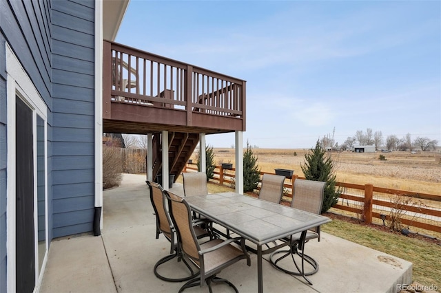 view of patio with a deck, outdoor dining area, a rural view, fence, and stairs