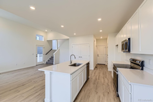 kitchen with sink, white cabinetry, stainless steel appliances, a center island with sink, and light wood-type flooring