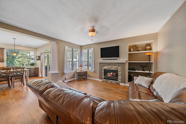 10421 Kennemere Ln, Parker, CO 80134 - living area with light wood finished floors, a stone fireplace, a ceiling fan, built in shelves, and decorative columns