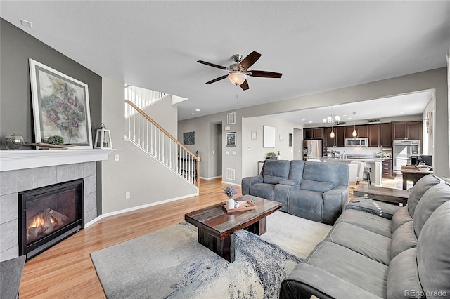 living room featuring a tiled fireplace, ceiling fan with notable chandelier, and light hardwood / wood-style floors