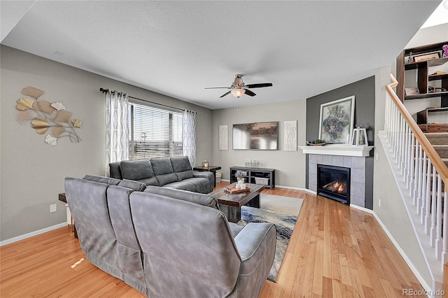 living room featuring ceiling fan, wood-type flooring, a tiled fireplace, and a textured ceiling