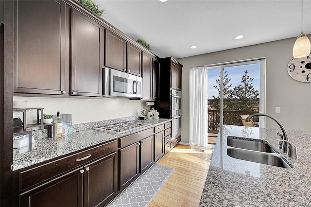 kitchen with appliances with stainless steel finishes, sink, hanging light fixtures, light stone counters, and dark brown cabinets