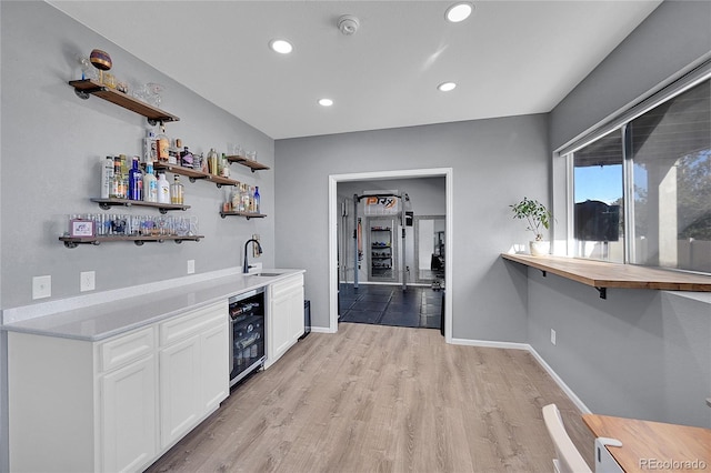 bar with beverage cooler, sink, light hardwood / wood-style flooring, and white cabinets