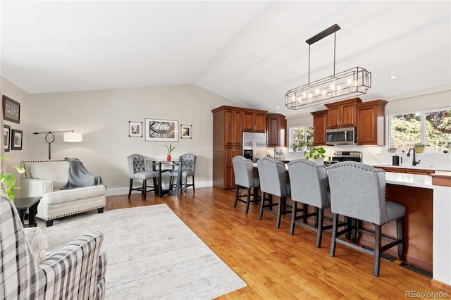 living area with an inviting chandelier, a healthy amount of sunlight, light wood-style flooring, and vaulted ceiling