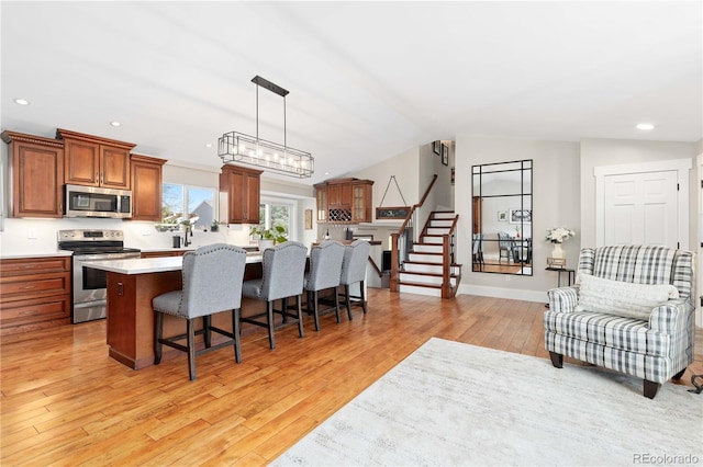 kitchen featuring a breakfast bar area, vaulted ceiling, light countertops, appliances with stainless steel finishes, and light wood-type flooring