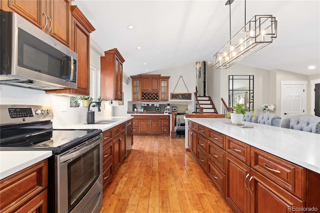 kitchen featuring light wood-style flooring, stainless steel appliances, vaulted ceiling, light countertops, and decorative light fixtures