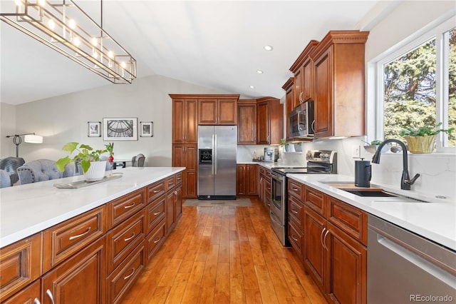 kitchen with light countertops, lofted ceiling, light wood-style flooring, appliances with stainless steel finishes, and a sink