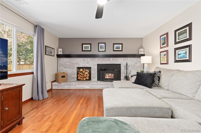 living area featuring a ceiling fan, light wood-style flooring, a fireplace, and baseboards