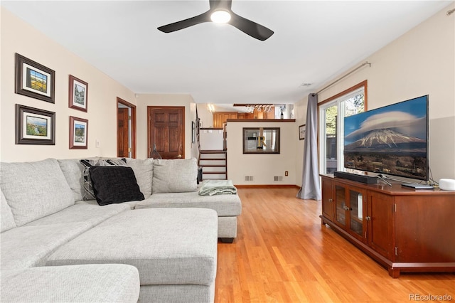 living area featuring visible vents, baseboards, stairway, light wood-style flooring, and a ceiling fan