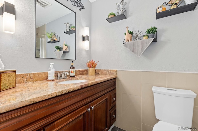 bathroom with visible vents, tile walls, toilet, a textured wall, and vanity