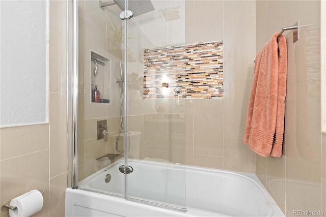 bathroom featuring tile walls and shower / bath combination with glass door