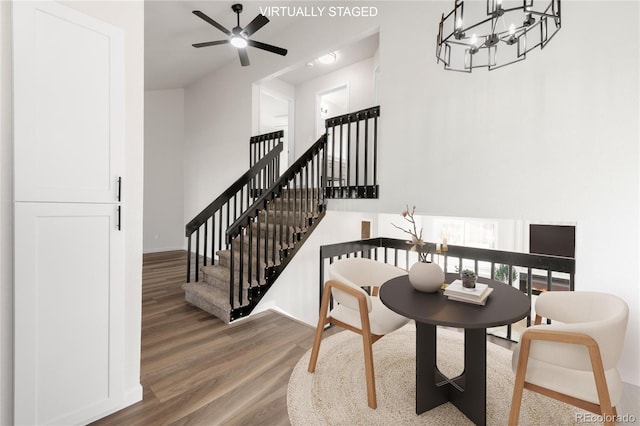 dining area with ceiling fan with notable chandelier, wood finished floors, baseboards, a towering ceiling, and stairs