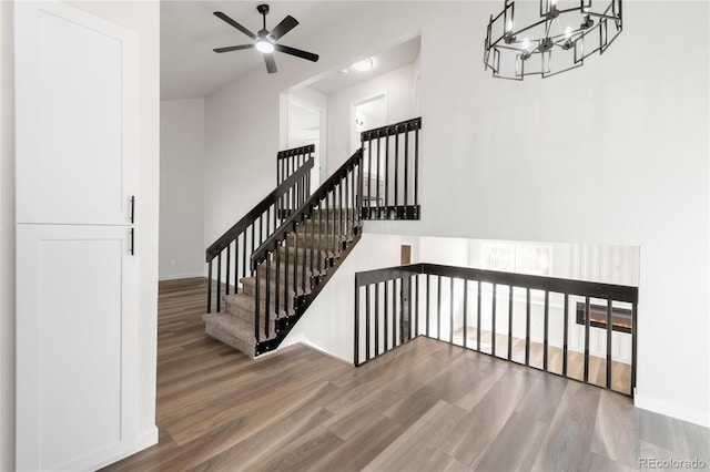 stairway featuring baseboards, a high ceiling, wood finished floors, and ceiling fan with notable chandelier