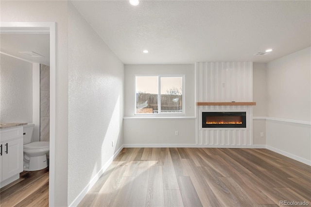 unfurnished living room featuring recessed lighting, light wood-type flooring, baseboards, and a glass covered fireplace