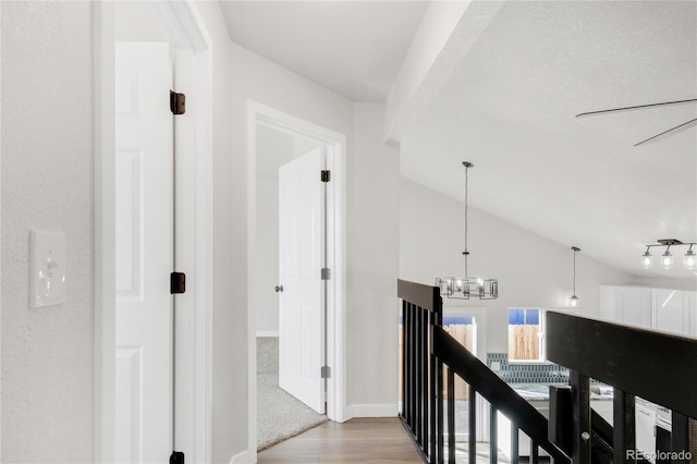 hall with lofted ceiling, light wood-style floors, baseboards, and a chandelier