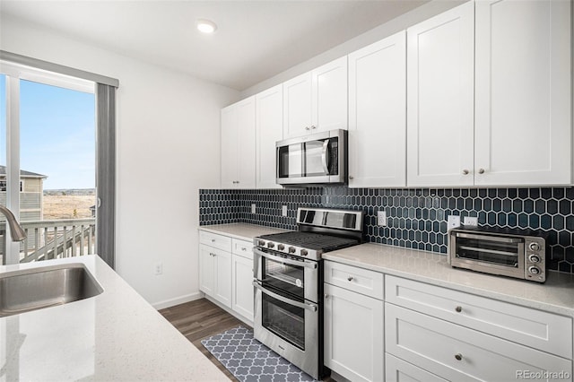 kitchen with dark wood-type flooring, stainless steel appliances, sink, white cabinets, and tasteful backsplash