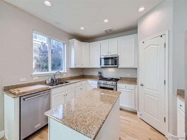 kitchen with light hardwood / wood-style floors, stainless steel appliances, white cabinets, sink, and a kitchen island