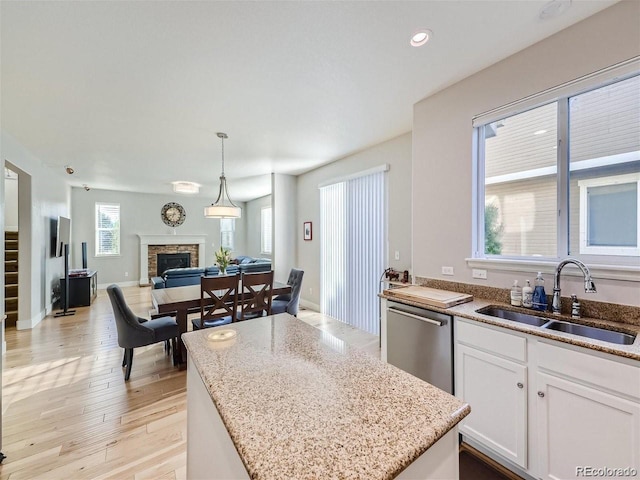 kitchen with a stone fireplace, light hardwood / wood-style floors, dishwasher, sink, and white cabinetry