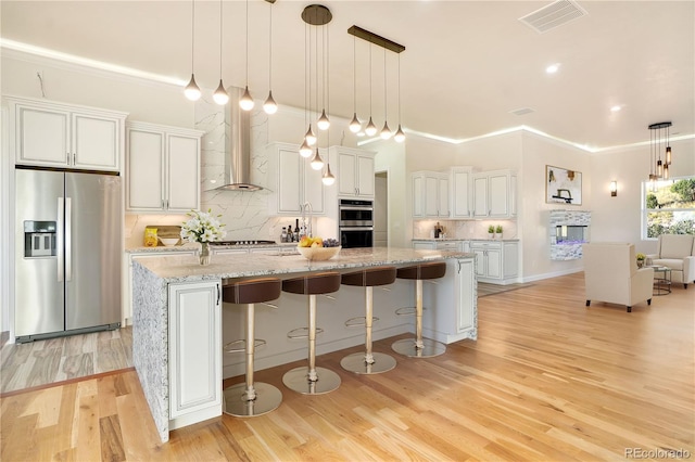 kitchen with appliances with stainless steel finishes, a large island, wall chimney range hood, and white cabinets