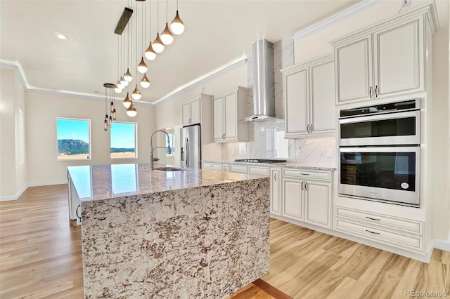 kitchen featuring pendant lighting, wall chimney range hood, a large island, stainless steel appliances, and light stone counters