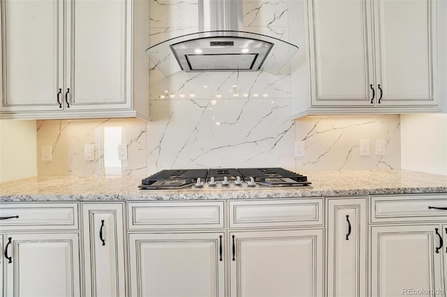 kitchen with island range hood, stainless steel gas stovetop, tasteful backsplash, white cabinets, and light stone counters