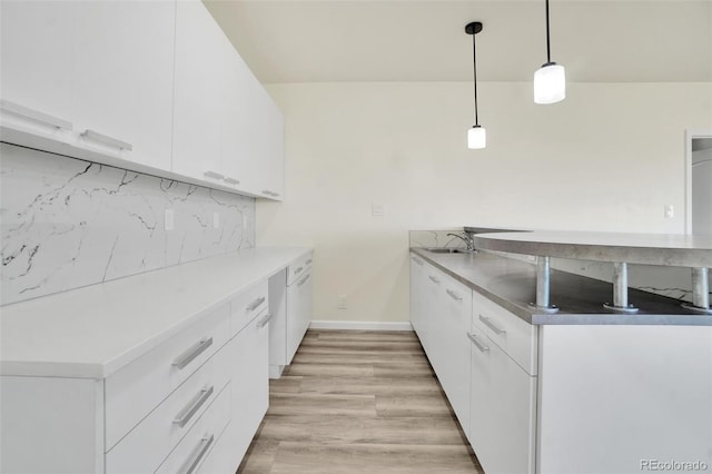 kitchen with backsplash, decorative light fixtures, white cabinets, and light wood-type flooring