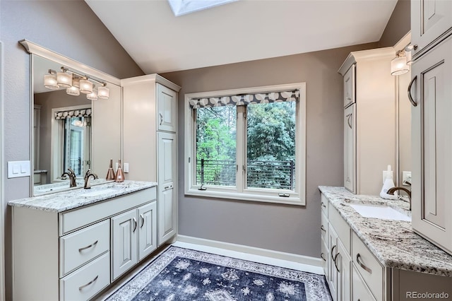 4856 Cheyenne Dr, Larkspur, CO 80118 - bathroom featuring two vanities, lofted ceiling, baseboards, and a skylight